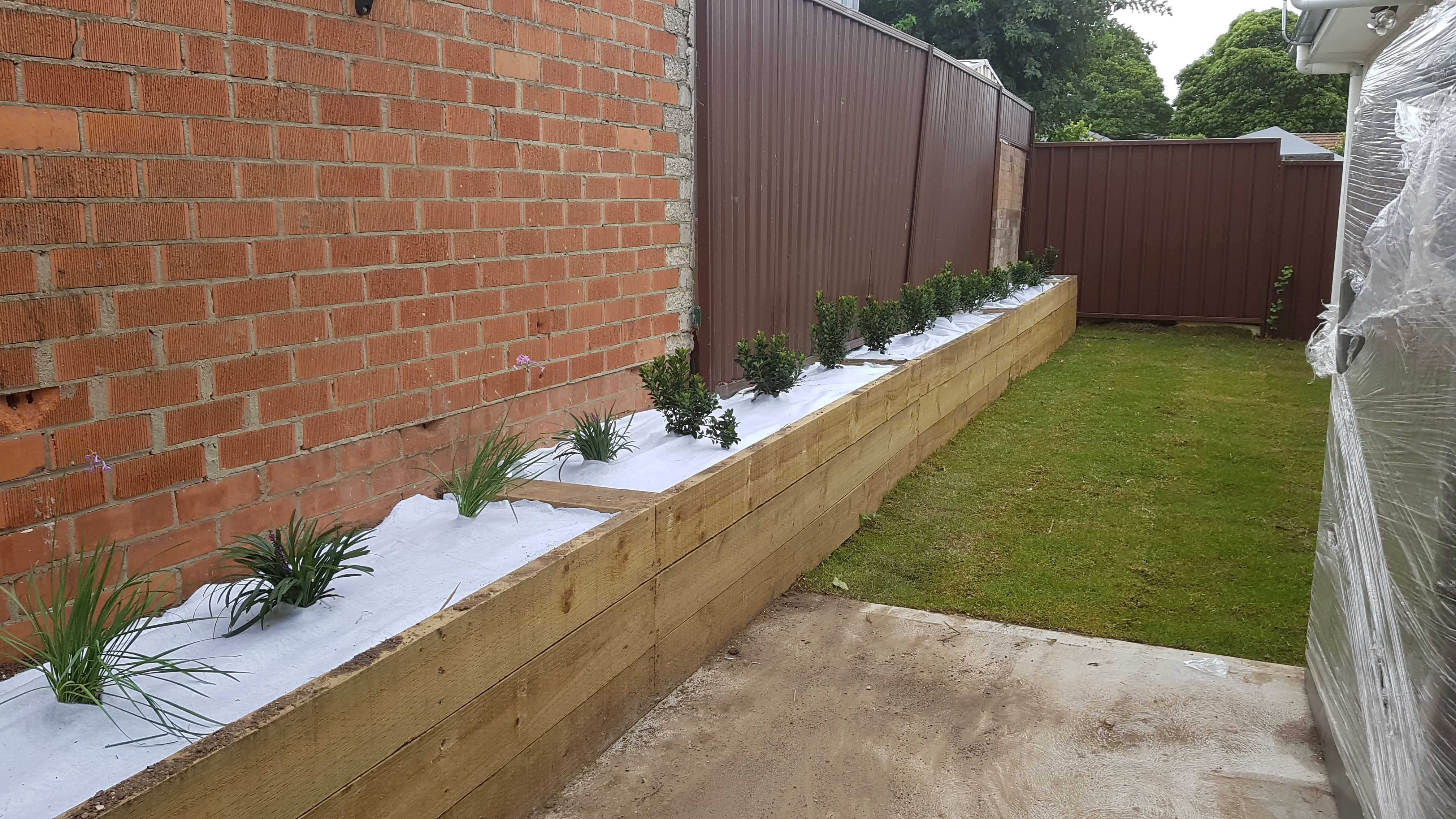 Long timber sleeper retaining bed with rows of new shrubs and grasses